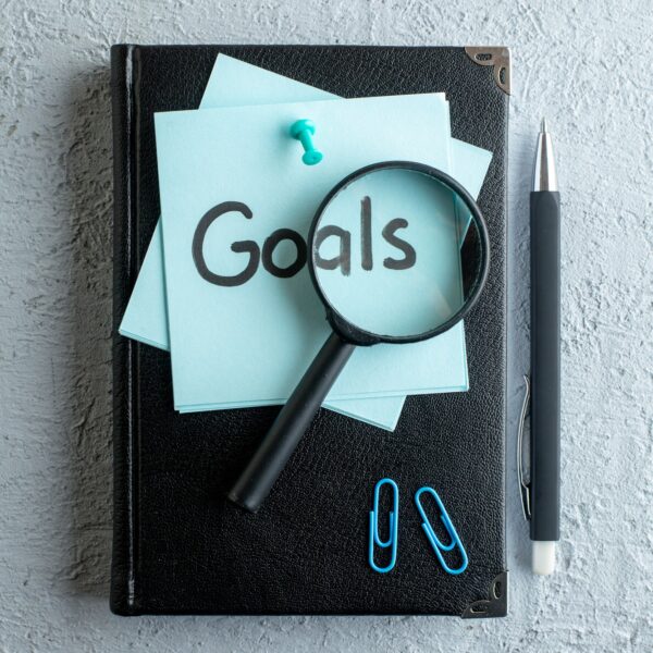 top-view-goals-written-note-with-notepad-pen-white-surface-job-office-school-copybook-color-college-business